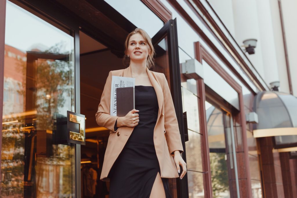 Young well dressed business woman with tablet pc leaving corporate building, hotel